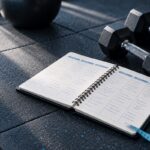Cuaderno con la planificación semanal de entrenamiento junto a unas mancuernas